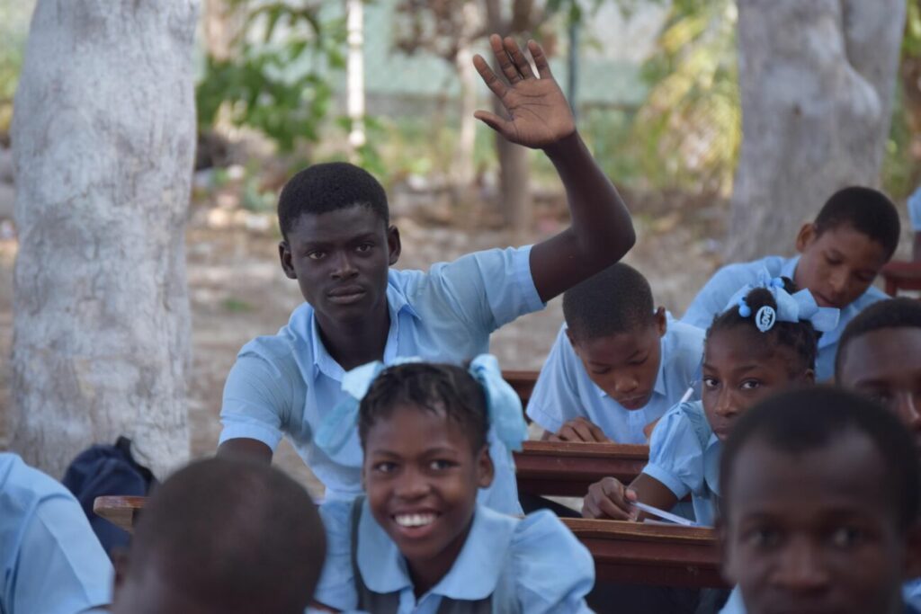 Un étudiant haïtien participe dans une des écoles de notre association en levant la main.