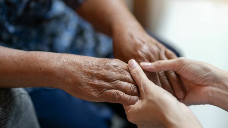 Une personne âgée tenant la main d'une personne jeune comme pour transmettre.